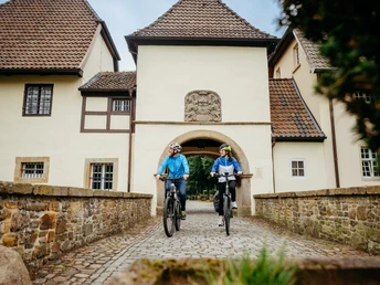 Radfahren auf der Artland-Rad-Tour Zwei Radfahrer passieren ein historisches Torhaus auf Kopfsteinpflaster.Two cyclists pass a historic gatehouse on cobblestones.To cyklister passerer et historisk porthus på brosten.Twee fietsers passeren een historisch poortgebouw op kasseien.