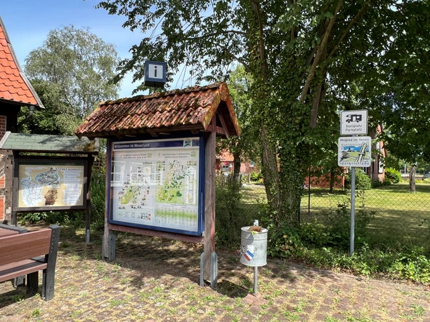 Touristisches Informationsschild auf einem mit Bäumen gesäumten Platz in Landesbergen mit Sitzbänken.