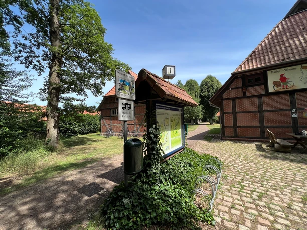 Estorfer Scheunenviertel Wohnmobilstellplatz Wohnmobilstellplatz mit Informationsschild und Fachwerkgebäuden, umgeben von Bäumen und gepflasterten Wegen.