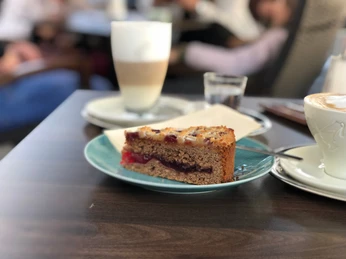 Kuchen Ein Stück Zwetschgenkuchen mit Streuseln auf einem grünen Teller, dahinter ein Glas mit Latte Macchiato.