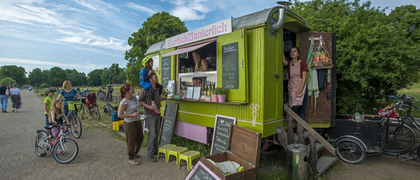 V parku je vidět celý vůz i několik zákazníků, kteří si něco objednávají, kavárna, catering, park, volný čas.