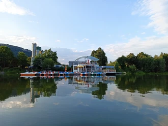 Wasserinn_freizeitgelaene_ahlemeyer.jpg Auf einem See schwimmendes Restaurant mit angelegten Tretbooten