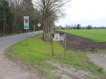 Infotafel über Atomkraft an einer Landstraße, flankiert von Bäumen und offenen Feldern bei bewölktem Himmel.