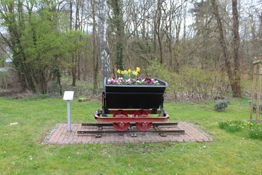Sandlore Eine historische Lore auf Gleisen, die mit bunten Frühlingsblumen bepflanzt ist, steht im Grünen.
