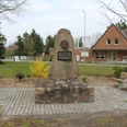 Gedenkstein in Lichtenhorst mit Büste und Inschrift, umgeben von Bänken und Landschaft.