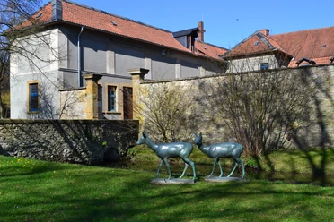 Haus Werther Skulpturen von zwei Hirschen vor einem steinernen Gebäude mit roten Ziegeldächern in ländlicher Umgebung.