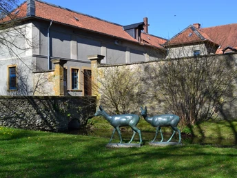 Haus Werther Skulpturen von zwei Hirschen vor einem steinernen Gebäude mit roten Ziegeldächern in ländlicher Umgebung.