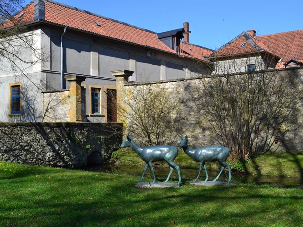 Haus Werther Skulpturen von zwei Hirschen vor einem steinernen Gebäude mit roten Ziegeldächern in ländlicher Umgebung.