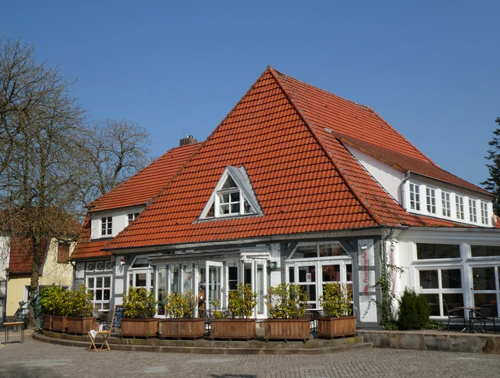 Ein Gebäude mit rotem Ziegeldach und großen Fenstern, umgeben von grüner Vegetation und blauen Himmel.