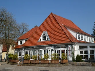 Alte Feuerwache Ein Gebäude mit rotem Ziegeldach und großen Fenstern, umgeben von grüner Vegetation und blauen Himmel.
