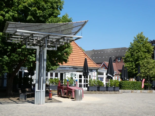 Feuerwache mit markantem Glockenspiel im Vordergrund, umgeben von Bäumen und blauem Himmel.