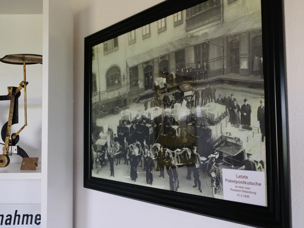 Postmuseum Bokel Das Bild zeigt ein gerahmtes historisches Foto im Postmuseum Bokel, mit der Aufschrift „Letzte Paketpostkutsche“ und verschiedenen Exponaten im Vordergrund. Die Ausstellung vermittelt einen Eindruck von der Geschichte der Postzustellung.