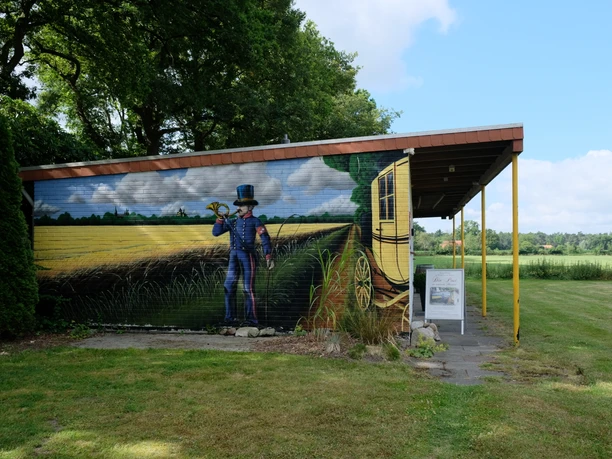 Postmuseum Bokel Das Gebäude des Postmuseums in Bokel mit einer großen Wandmalerei eines Postboten und einer Kutsche.