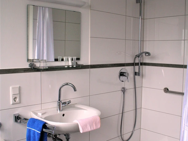 Barrierefreies Badezimmer mit bodengleicher Dusche, Haltegriffen und Waschbecken mit Handtuchhalter.