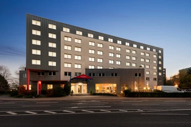 Modernes sechsstöckiges Hotelgebäude mit beleuchteten Fenstern und Eingang bei Abenddämmerung