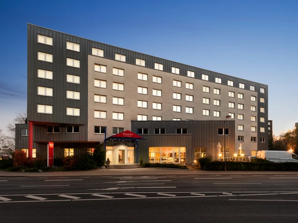 Modernes sechsstöckiges Hotelgebäude mit beleuchteten Fenstern und Eingang bei Abenddämmerung