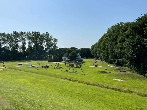 Kinderspielplatz am Deich Spielplatz auf großer Wiese neben Bäumen am Deich