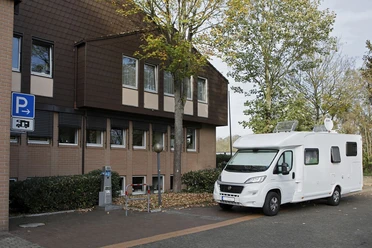 Wohnmobilstellplatz am Borchener Rathaus Stellplatz für Wohnmobile neben einem Gebäude mit Bäumen und Parkautomat, herbstliche Umgebung.