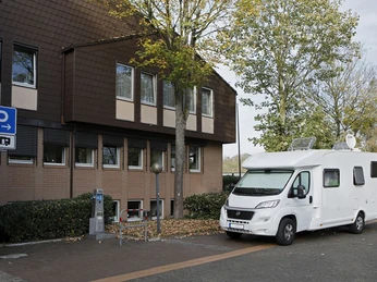 Wohnmobilstellplatz am Borchener Rathaus Stellplatz für Wohnmobile neben einem Gebäude mit Bäumen und Parkautomat, herbstliche Umgebung.