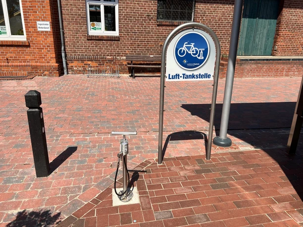 Lufttankstelle Bruchhausen Ein Fahrradluftpumpgerät steht vor einem Backsteingebäude, flankiert von einem Luftradzeichenschild.