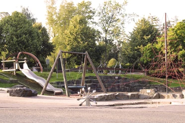 Spielplatz Herminghauspark in Velbert Ein großzügiger Spielplatz mit Schaukeln, Rutsche und Klettergerüst, umgeben von viel Grün.