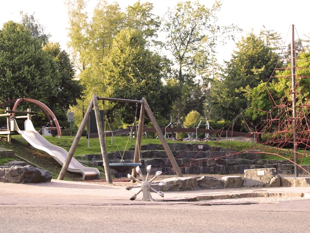 Spielplatz Herminghauspark in Velbert Ein großzügiger Spielplatz mit Schaukeln, Rutsche und Klettergerüst, umgeben von viel Grün.