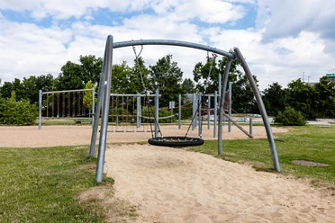 Spielplatz Am Sandbach in Ratingen Ein moderner Spielplatz mit Klettergerüsten und Schaukeln, umgeben von grünen Bäumen und Wiesen.