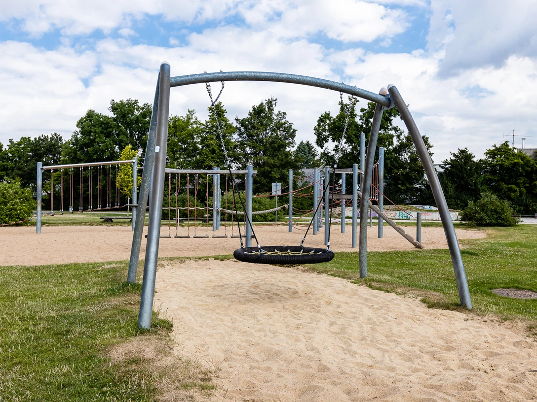 Spielplatz Am Sandbach in Ratingen Ein moderner Spielplatz mit Klettergerüsten und Schaukeln, umgeben von grünen Bäumen und Wiesen.