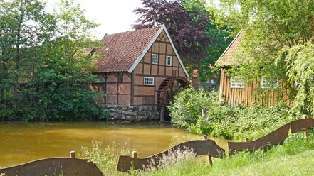 Wassermühle Bruneforth in Stavern ©Emsland Tourismus GmbH (4).JPG Fachwerk-Wassermühle mit großem Holzwasserrad an einem Teich, umgeben von dichtem Grün und Bäumen.