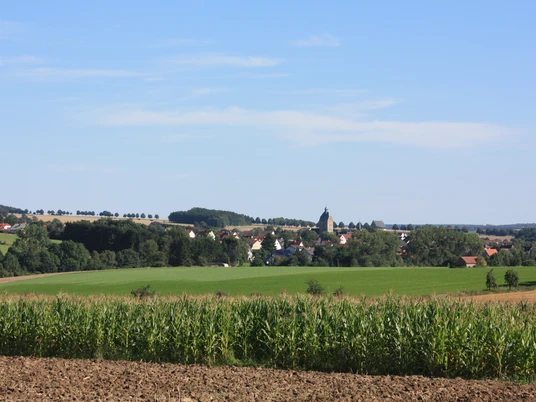 Blick auf das Dorf Lichtenau, eingebettet in grüne Felder und umgeben von sanften Hügeln.
