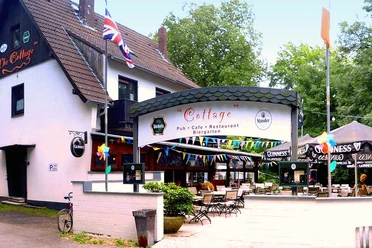 cottage-bottrop-6.jpg Eingangsbereich des Cottage Pub in Bottrop mit Biergarten, bunten Fahnen und Außensitzplätzen.