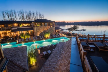 Vabali Spa in Hilden Ein modernes Spa mit Außenpool, umgeben von üppigem Grün und entspannender Flusslandschaft in der Abenddämmerung.
