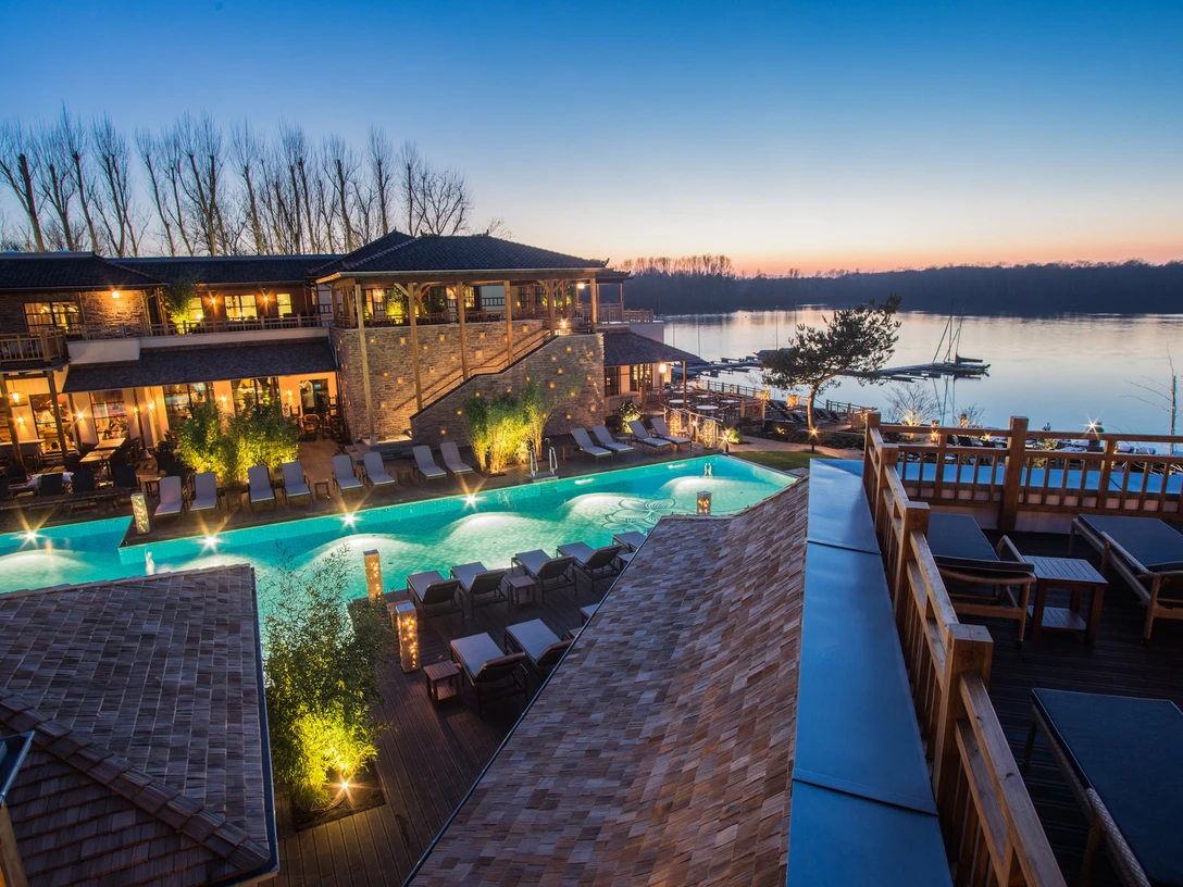 Vabali Spa in Hilden Ein modernes Spa mit Außenpool, umgeben von üppigem Grün und entspannender Flusslandschaft in der Abenddämmerung.