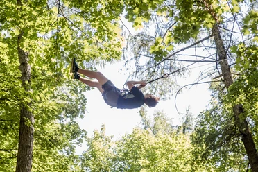 Waldkletterpark Velbert-Langenberg Eine Person schwingt fröhlich an einem Seil zwischen den grünen Baumkronen im Waldkletterpark.