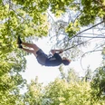 Waldkletterpark Velbert-Langenberg Eine Person schwingt fröhlich an einem Seil zwischen den grünen Baumkronen im Waldkletterpark.