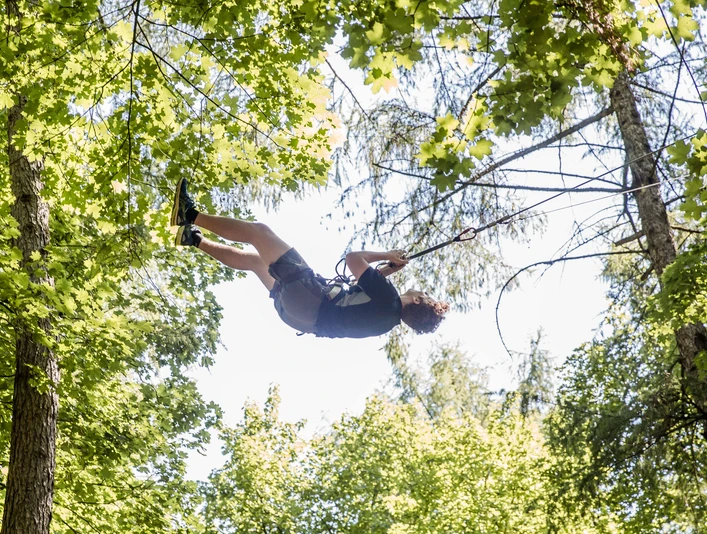 Waldkletterpark Velbert-Langenberg Eine Person schwingt fröhlich an einem Seil zwischen den grünen Baumkronen im Waldkletterpark.