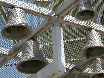 Sechs große, teils schattige Glocken hängen in einem Metallgerüst gegen den blauen Himmel.