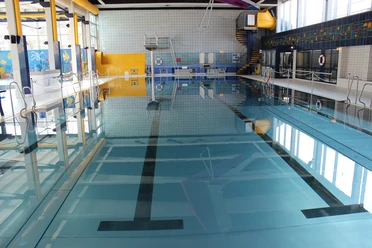Wülfrather Wasserwelt Modernes Schwimmbecken mit blauen Fliesen, Wasserrutsche und lichtdurchfluteten Fenstern im Hallenbad.