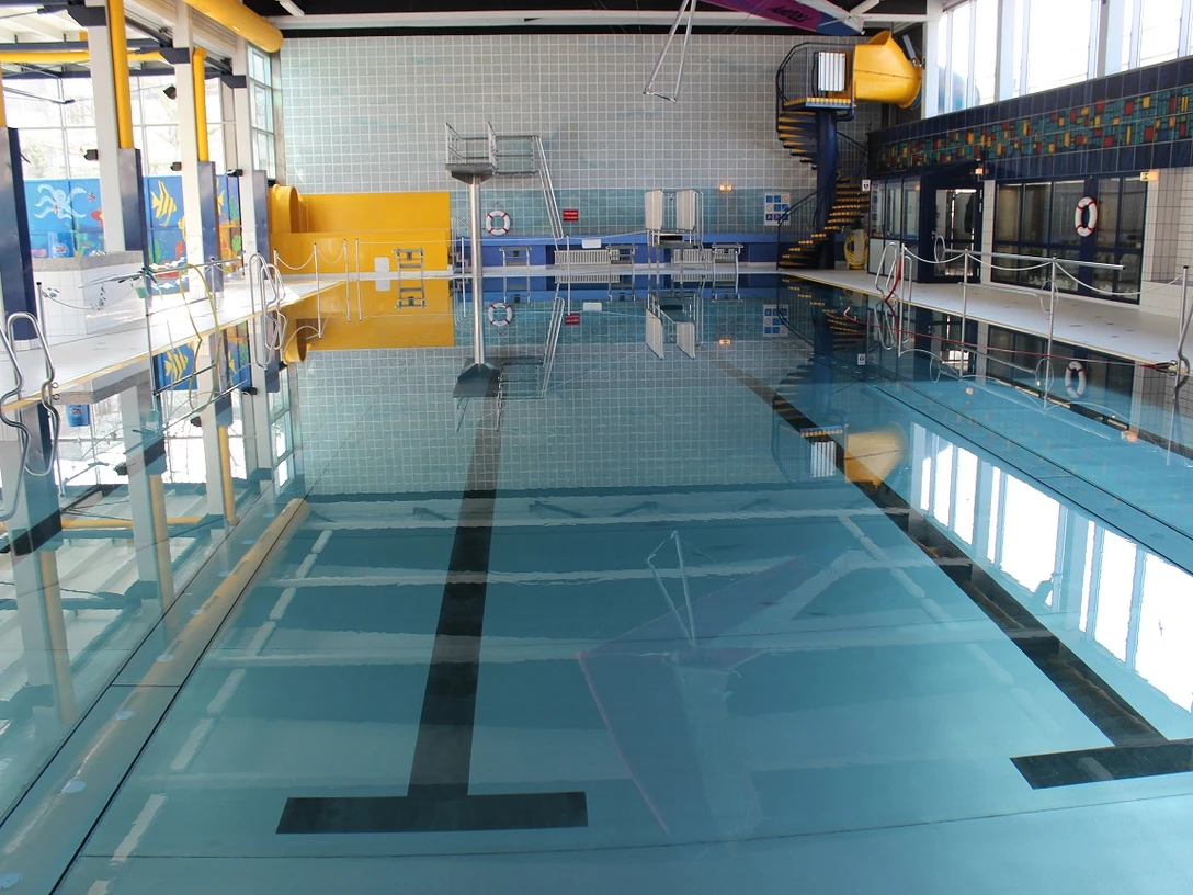 Wülfrather Wasserwelt Modernes Schwimmbecken mit blauen Fliesen, Wasserrutsche und lichtdurchfluteten Fenstern im Hallenbad.
