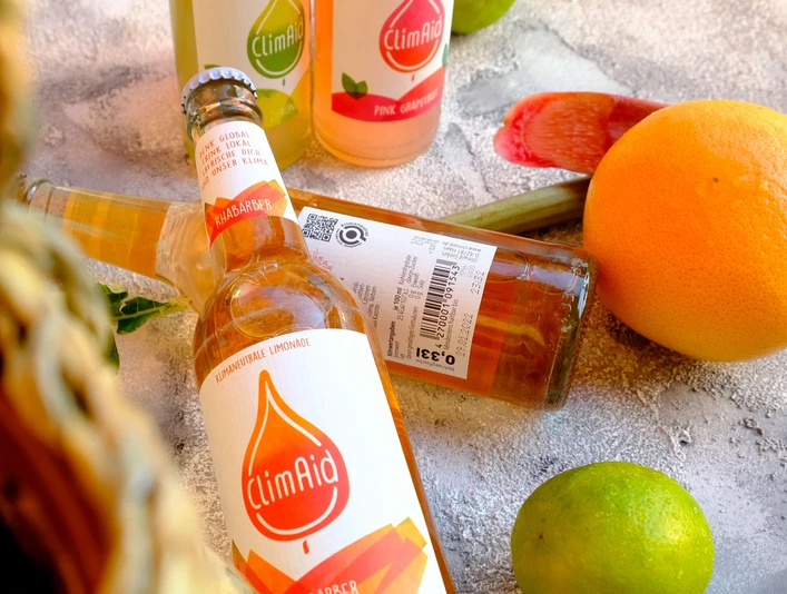 ClimAid Limonaden aus Haan ClimAid Limonadenflaschen liegen vor verschiedenen Zitrusfrüchten und versprechen erfrischenden Genuss.