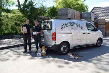 Gut Grashaus aus Ratingen Zwei Mitarbeitende stehen lächelnd neben einem Lieferwagen von Gut Grashaus, umgeben von Tierfutter.
