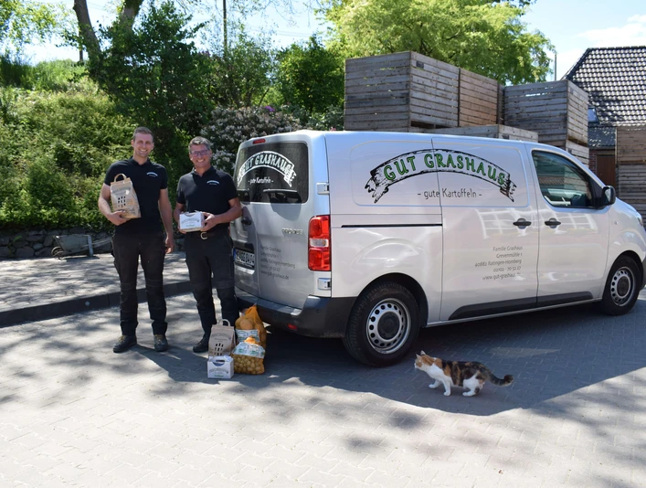 Gut Grashaus aus Ratingen Zwei Mitarbeitende stehen lächelnd neben einem Lieferwagen von Gut Grashaus, umgeben von Tierfutter.