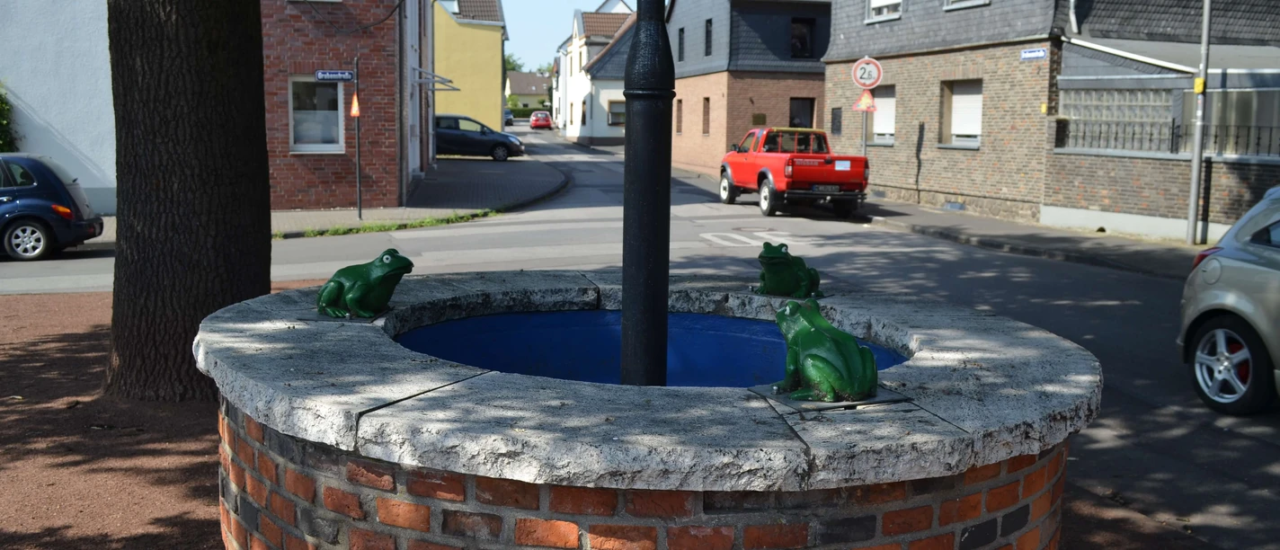 Kradepohl in Monheim am Rhein Ein runder Brunnen aus Ziegelsteinen mit Froschfiguren steht an einer Straßenkreuzung in Monheim am Rhein.