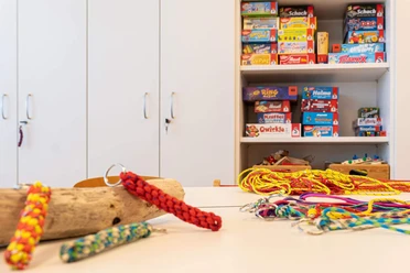 Basteln im Mini-Maxi-Club Bunte Schlüsselanhänger liegen auf dem Tisch. Im Hintergrund sind im Schrank Spiele zu sehen.