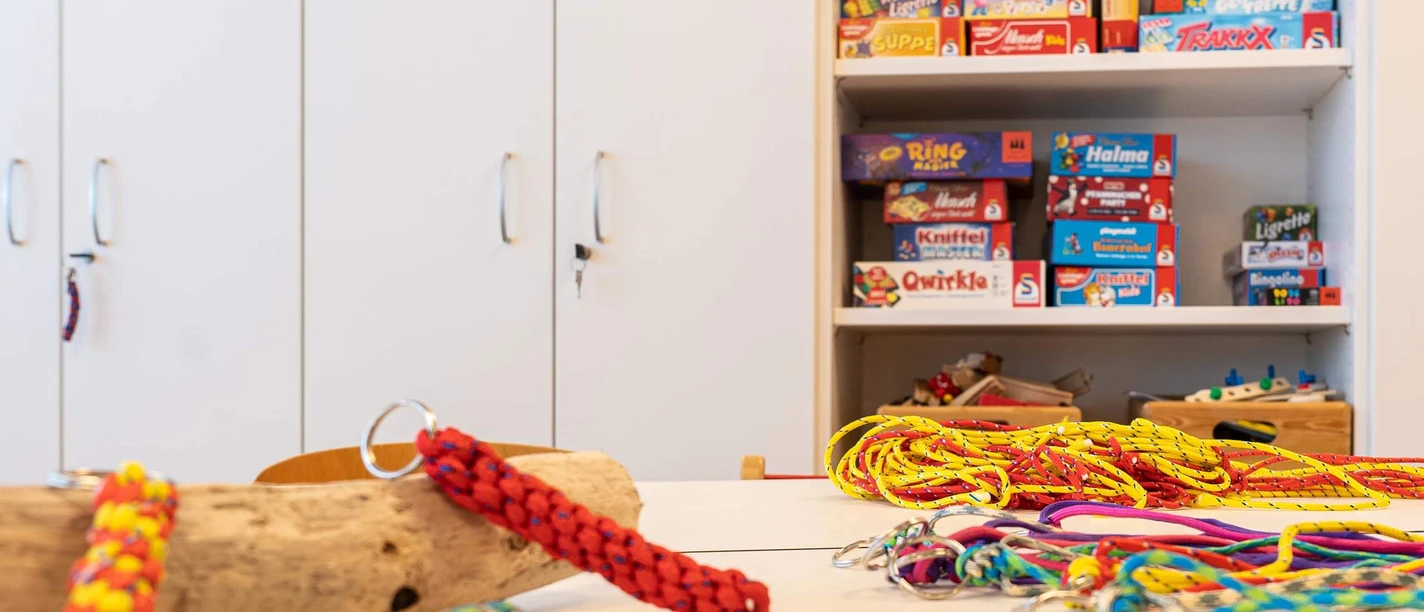 Basteln im Mini-Maxi-Club Bunte Schlüsselanhänger liegen auf dem Tisch. Im Hintergrund sind im Schrank Spiele zu sehen.
