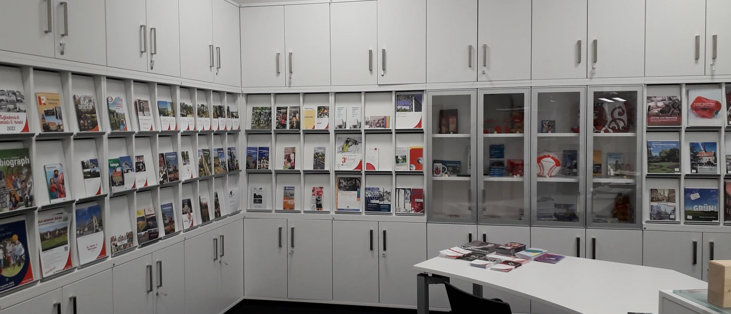 Tourist-Information Ratingen Reiseführer und Broschüren in einem Informationszentrum mit weißen Schränken und einem Tisch.