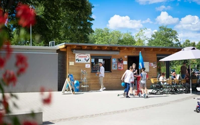Tourist-Information Giebner in Monheim am Rhein Tourist-Information mit Holzverkleidung, Menschen und Fahrradführungen, umgeben von grünem Park.
