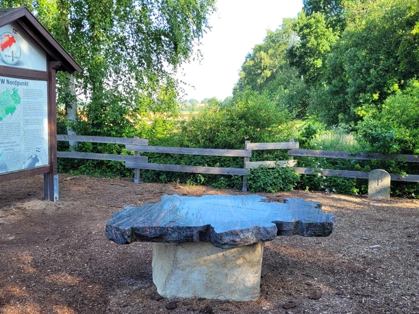 Steinrelief in Form von Nordrhein-Westfalen, umgeben von Bäumen und Holzzaun im Grünen.