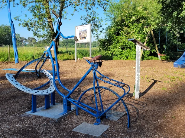 NRW Nordpunkt Blaues Fahrraddenkmal im Freien, umgeben von grünen Bäumen, nahe einem Feldweg.