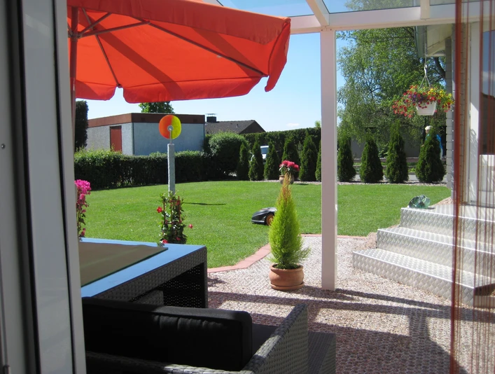 Terrassenausblick .JPG Sonnige Terrasse mit rotem Sonnenschirm, Blick auf gepflegten Garten und Rasen, moderne Sitzmöbel.